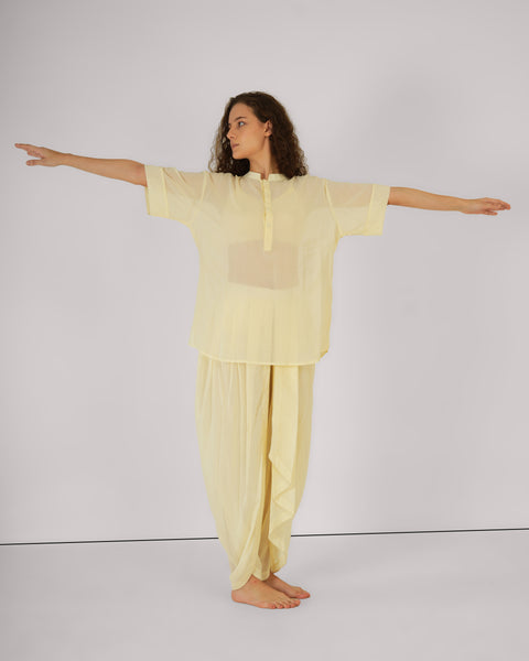 Woman in soft yellow YogaFlow set standing with arms outstretched — 100% cotton, airy and centered in open-bodied stillness.