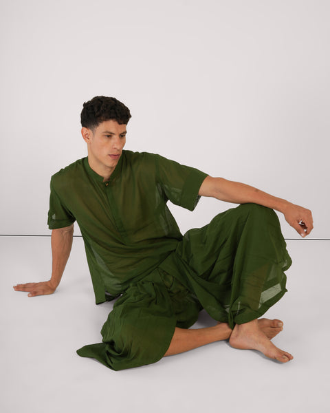 Male seated casually on studio floor in Mehndi green 100% cotton yoga set, relaxed pose, breathable natural fabric, white background.