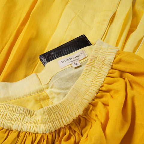 Close-up of Shanti Chola label on Saffron Sunrise pants — linen cotton fabric with gathered waistband, hand-dyed in radiant yellow tones.